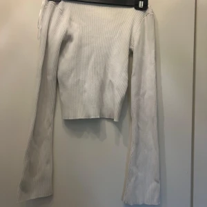 Vit ribbad croppad tröja - Superfin vit ribbad tröja med croppad passform och långa ärmar. Tröjan har en snygg offshoulder-ringning som ger en trendig vibe. Perfekt till jeans eller kjol för en chill och stilren look.