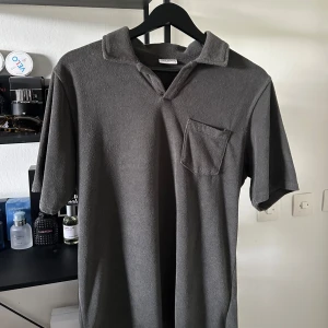 Grå pikétröja från John Henric - Snygg grå pikétröja från John Henric med klassisk krage och bröstficka. Tröjan har korta ärmar och är tillverkad i ett mjukt, frottéliknande material som ger en chill vibe. Perfekt för dig som gillar stilren och enkel design.