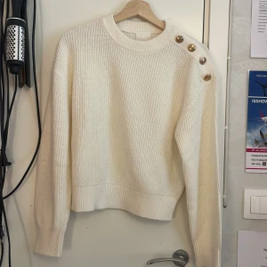En krämvit stickad tröja från H&M med guldiga knappar  - Säljer en stickad tröja från H&M för den kommer aldrig till användning💕. Strl XS. Nytt skick har bara använt en gång🩷. Köparen får betala för frakten 