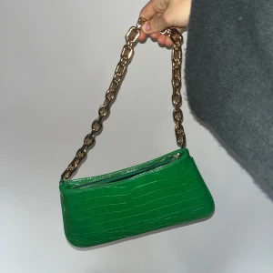 Grön axelväska med kedja - Snygg grön axelväska i croco-mönstrad syntet med chunky guldfärgad kedja som axelrem. Väskan har dragkedja upptill och en stilren, avlång form som ger en trendig vibe. Perfekt för dig som vill sticka ut med färg och coola detaljer.💕💕💕😃😃