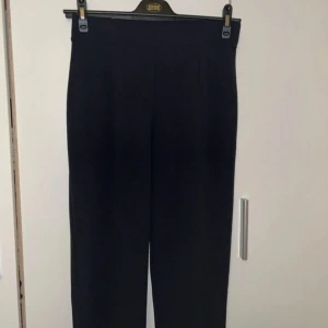 Mörkblå byxor från H&M, stl M - Ett par byxor i kraftig trikă med hög midja med resår och avsmalnande ben med pressveck fram och bak. Insida ben: Längd: 68.0 cm (Storlek M) Färg: Mörkblå I använt men fin skick.