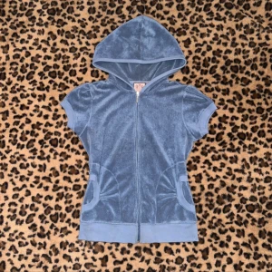 Blå velour hoodie Juicy Couture S - Blå kortärmad hoodie från Juicy Couture i mjuk velour. Tröjan har dragkedja framtill, huva och två fickor med snygga detaljer. Perfekt för en chill och trendig look.