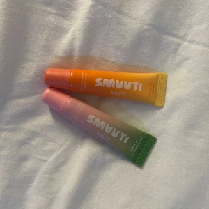 Smuuti Skin läppmask duo - Två läppmasker från Smuuti Skin i tub, en med persikosmak i orange och en med vattenmelonsmak i rosa/grön. Båda innehåller extrakt och ceramider för återfuktning. Perfekt för mjuka läppar och snyggt färgglada förpackningar.