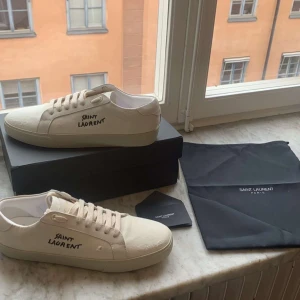 Saint Laurent vita sneakers i canvas - Snygga vita sneakers från Saint Laurent i canvas med handskriven logga på sidan. Klassisk låg modell med rund tå, platt sula och vita snören.Perfekta för en clean och stilren look. Kommer med originalbox och dustbag.