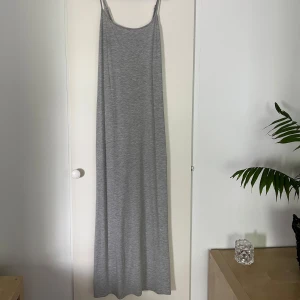 Grå långklänning med smala axelband - En lång maxiklänning från GinaTricot i en ljusgrå färg. Edast använt fåtal gånger. Klänningen sitter tight mot kroppen men har ändå ett stretchigt material. 