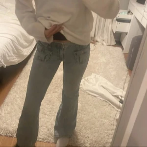 Ljusblå bootcut jeans - Säljer ett par ljusblå jeans med bootcut-modell och låg midja. Jeansen har klassiska fickor fram och bak samt en snygg, lätt utsvängd passform nertill. Perfekta för dig som gillar en retro vibe och vill ha ett par jeans som sticker ut lite extra.