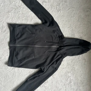 Svart oversize hoodie med dragkedja från 157 - Svart hoodie från 157 i storlek XS. Tröjan har hel dragkedja framtill, två fickor och justerbar huva med snören. Tillverkad i mjukt material som känns skönt mot huden. Perfekt för lager-på-lager och chill dagar. Använd 1 gång 