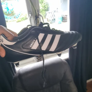 Adidas copa mondial - Klassiska Adidas Kaiser 5 fotbollsskor i svart skinn med vita detaljer och de ikoniska tre ränderna på sidan. Skorna har snörning och utbytbara dobbar i metall för grymt grepp på planen. Perfekta för dig som vill ha en tidlös och stilren look på matchen. Spillrans nya köpta nya i Frankrike aldrig använda