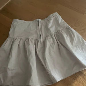 Beige volangkjol från Holly & Whyte - Supersöt beige kortkjol från Holly & Whyte med volang och dragkedja bak. Kjolen har en lätt utsvängd form och är perfekt för dig som gillar en enkel men trendig look. Tillverkad i bomull för en skön känsla.