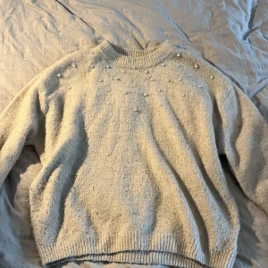 Beige stickad tröja med pärlor - Beige stickad tröja med pärldetaljer över axlar och bröst. Storlek 146/152