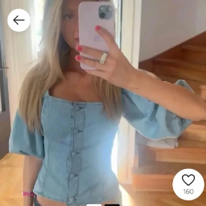 Ljusblå jeanskorsett med puffärm - Superfin ljusblå korsettopp i jeans med puffiga trekvartsärmar och knappar framtill. Snygg fyrkantig urringning och figurnära passform som ger en cool och trendig vibe. Perfekt att styla med höga jeans eller kjol för en extra edge. Priset går att diskutera!