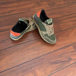 Valentino sneakers i grönt och orange - Snygga sneakers från Valentino i militärgrönt tyg och mocka med orange detalj på hälen. Hör gärna av er om ni är intresserade att köpa
