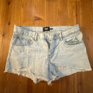 Ljusblå jeansshorts från 157 - Snygga ljusblå jeansshorts från 157 med fransig, rå kant och klassisk femficksmodell. Shortsen har normal passform och är perfekta för varma dagar. De är tillverkade i mjukt denim och har bälteshällor och knappgylf.