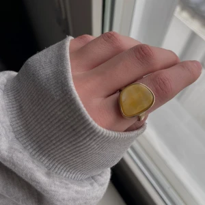 Gul statementring i guldtonad metall - Säljer en snygg ring med stor, gul sten i triangulär form och guldtonad infattning. Perfekt för dig som vill ha ett unikt smycke som sticker ut.