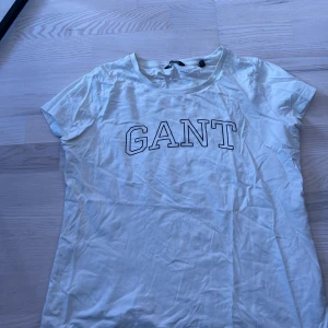 Vit t-shirt från GANT - Vit t-shirt från GANT med klassisk rund halsringning och tryckt GANT-logga på bröstet. Enkel och stilren design, perfekt till jeans eller shorts. Tillverkad i mjuk bomull för en bekväm känsla.