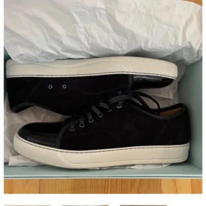 Svarta sneakers med nitar och röd sula - Säljer ett par svarta sneakers från Christian Louboutin med ikonisk röd sula och svarta nitar framtill. Skorna har snörning och en rund tå. Perfekta för dig som vill sticka ut med en edgy stil.
