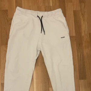 Vita mjukisbyxor från Hugo - Vita mjukisbyxor från Hugo med svart dragsko i midjan och diskret logga på ena benet. Byxorna har en avslappnad passform och resår i midjan för extra komfort. Perfekta för chill dagar eller när du vill ha det bekvämt.