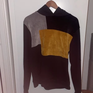 Flerfärgad hoodie från La Vichy - Säljer en snygg hoodie från La Vichy i sammet med färgblock i svart, grått och senapsgult. Tröjan har långa ärmar och en skön huva. Perfekt för dig som gillar en unik och trendig stil.
