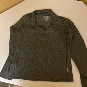 Mörkgrå långärmad träningströja från Ravelli - Säljer en mörkgrå långärmad träningströja från Ravelli i storlek XXS. Tröjan har halv dragkedja framtill och är tillverkad i ett stretchigt material av polyester och elastan. Perfekt för träning eller aktiva dagar.