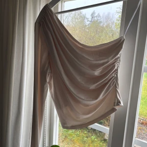 Beige vit topp - Säljer en super fin beige vit topp med en  arm i satinmaterial från H&M. Den är helt oanvänd och lappen är kvar. 
