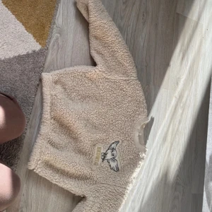 Beige teddytröja med Hedwig-broderi från H&M - Supermjuk och fluffig beige teddytröja från H&M med broderad Hedwig-uggla framtill. Tröjan har lång ärm och ribbad krage. Perfekt för dig som gillar Harry Potter och vill ha något riktigt mysigt på dig.