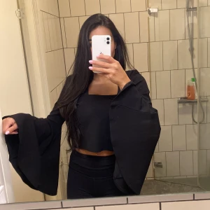 Svart croppad topp med vida ärmar från ZARA - Säljer en svart croppad topp från ZARA med långa, extra vida ärmar. Toppen har en fyrkantig urringning och är tillverkad i ett mjukt material. Perfekt för dig som vill sticka ut med en trendig och stilren look.