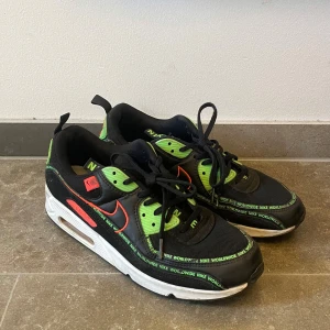 Nike Air Max 90 Worldwide svart/grön - Säljer ett par Nike Air Max 90 Worldwide i svart med gröna och röda detaljer. Skorna har snörning, vit sula med synlig Air Max-enhet och texten 'NIKE WORLDWIDE' längs kanterna. Perfekta för dig som gillar unika sneakers med färg. Pricet kan förhandlas vid snabb affär 