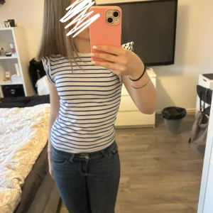 Vit och blå randig t-shirt - Säljer en klassisk vit t-shirt med blå horisontella ränder. T-shirten har rund halsringning och korta ärmar. Perfekt till jeans eller shorts för en avslappnad stil.