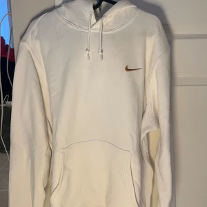 Vit hoodie från Nike - Säljer en klassisk vit hoodie från Nike med brunt swoosh-broderi på bröstet. Pris går att diskutera 