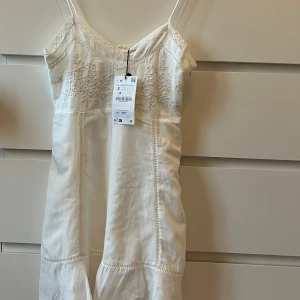 Vit sommarklänning  - Söt vit miniklänning från Zara med tunna axelband och v-ringning. Broderade detaljer upptill och lätt volang nertill. Klänningen är mycket kort.