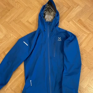 Blå Haglöfs L.I.M Series Gore-Tex jacka - Säljer en blå skaljacka från Haglöfs L.I.M Series med Gore-Tex-material. Jackan har huva, dragkedja framtill och en bröstficka med dragkedja. Perfekt för utomhusaktiviteter när du vill hålla dig torr och skyddad mot väder. Perfekt condition! Öppen för byten 🕺🏼😎