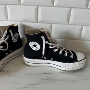 Svarta Converse All Star platform sneakers - Säljer ett par klassiska svarta Converse All Star med vit platåsula och högt skaft. Skorna har vita snören, rund tå och tydlig logga på sidan. Perfekta för dig som vill ha en tidlös och cool stil. Kan torka av sulan