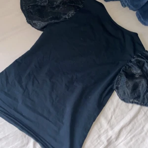 Svart topp med puffärmar från Lindex - Säljer en svart topp från Lindex i storlek XS. Toppen har unika puffärmar i transparent tyg som ger en snygg och trendig look. Perfekt att styla till olika outfits. Materialet känns mjukt och bekvämt mot huden.