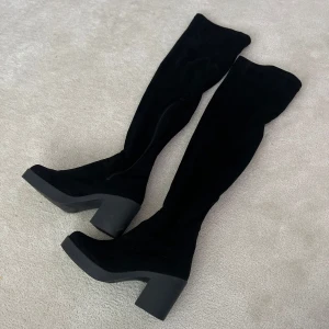 Svarta overknee stövlar med klack - Säljer ett par svarta overknee stövlar med hög klack och rund tå. Skorna har en stilren design och är tillverkade i ett mjukt material som ger en snygg passform längs benet. Perfekta för att lyfta vilken outfit som helst.