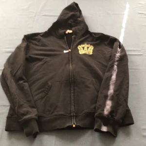 Svart hoodie från Juicy Couture med guldkrona - Svart vintage hoodie från Juicy Couture med dragkedja och huva. Stor guldkrona i tryck på ryggen och mindre krona på bröstet. Mjukt material och ribbade muddar vid ärmslut och nederkant.