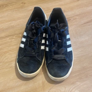Adidas Campus svart/vit strl 38 2/3 – stilrena sneakers! - Svarta Adidas Campus sneakers med de ikoniska vita ränderna på sidorna och vit hälflik med Adidas-logga. Skorna har snörning och en platt sula – perfekta för en avslappnad och stilren look. Storlek: 38 2/3 Använda men i fint skick – inga hål eller större skador, endast vanligt slitage. Nypris ca 500/1000 kr. Pris: 150 kr hör av dig vid frågor!