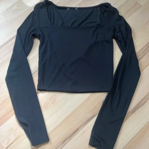 Svart långärmad topp med fyrkantig ringning - En stilren svart långärmad topp med fyrkantig ringning. Perfekt att matcha med både jeans och kjol för en trendig look. Tunn och mjuk i materialet, sitter snyggt. Från new yorker i stl xs