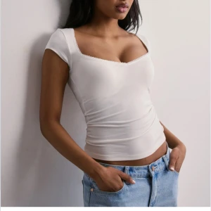 Vit croppad topp med fyrkantig ringning - Säljer en vit croppad topp med korta ärmar och snygg fyrkantig ringning. Toppen är tight och har en enkel, stilren design som passar perfekt till jeans eller kjol. Materialet är mjukt och stretchigt för en bekväm passform. Aldrig använd då jag köpt fel strlk 