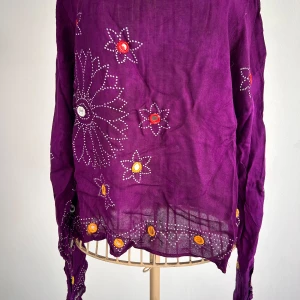 Lila långärmad topp med broderade blommor  - Lila, unik långärmad croppad topp med broderade blommor i olika färger. Stick ut i mängden med denna topp. Saknar ’speglar’ i några blommor på ärmarna men inget som stör, se sista bilden. Uppskattar den till Stl m. 