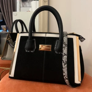Svart och vit handväska från River Island - Stilren handväska från River Island i svart och vitt med en axelrem i ormmönstrad stil. Väskan har två handtag, dragkedja upptill och hårdare struktur. 