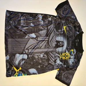 Nike Brasil Dri-Fit fotbollströja svart - Unik svart Brasilien fotbollströja från Nike med Dri-Fit-material. Framsidan har ett detaljerat grafiskt tryck med Kristusstatyn och brasilianska symboler, samt CBF-emblem i gult. Korta ärmar och rund hals. Perfekt för dig som vill sticka ut på planen.