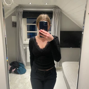 Svart ribbad topp med spets från Amisu - Supersnygg svart långärmad topp från Amisu i ribbat material. Djup v-ringning både fram och bak med fina spetsdetaljer längs kanterna.