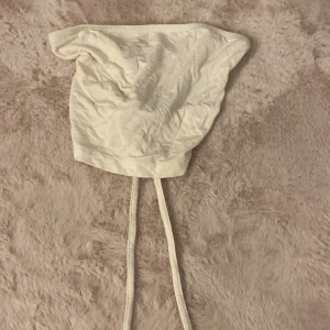 Vit bandeau tubtopp med snörning - Säljer en vit bandeau tubtopp med snygg snörning i ryggen. Toppen är ärmlös och har en enkel, stilren design som passar perfekt till sommarens outfits. Gjord i mjukt bomullstyg. 