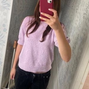Ljuslila stickad topp Vero Moda XS - Superfin ljuslila stickad tröja från Vero Moda i storlek XS. Tröjan har korta puffärmar och ribbade muddar vid ärmslut och nederkant. Mjuk och skön, perfekt till både jeans och kjol. Enkel men ändå söt med sin puffiga ärm och pastelliga färg.