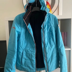 Blå vinterjacka från Phenix med huva - Säljer en blå vinterjacka från Phenix med orange dragkedja och huva. Jackan har värmande Thunderon Digenite Thermo-foder och patch på ärmen. Perfekt för kalla dagar och snygg sportig look. Kan diskutera pris. 