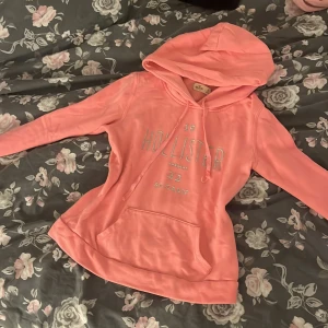 Rosa Hollister hoodie - Supermjuk rosa hoodie från Hollister med broderad logga framtill. Tröjan har huva med snörning, magficka och långa ärmar. Perfekt för chill dagar och snygg att matcha med jeans eller leggings. Storlek XS, typ aldrig använd.