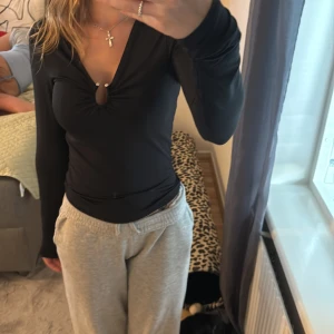 Svart kortklänning med v-ringning - Supersnygg svart kortklänning med lång ärm och djup v-ringning framtill. Klänningen har en cool detalj med rynk och liten cut-out vid bysten. Sitter tight och framhäver figuren, perfekt för dig som gillar en stilren men ändå trendig look.