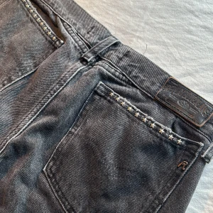 Replay low rise svarta jeans med stjärndetaljer - Snygga svarta Replay jeans med slitna benslut och coola stjärn-nitar vid fickorna. Jeansen har klassisk femficksmodell och en tvättad svart färg som ger en vintagekänsla. 