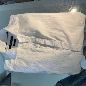 Vit skjorta från Tiger of Sweden - Klassisk vit skjorta från Tiger of Sweden i storlek 38. Skjortan är tillverkad i bomull, har lång ärm, knappar framtill och stilren krage. Perfekt för dig som gillar en clean och tidlös look. Snygg passform och enkel att matcha med jeans eller kostymbyxor.