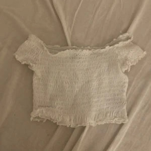 Vit smockad croppad topp H&M Divided XS - Superfin vit croppad topp från H&M Divided i storlek XS. Toppen är smockad med elastisk struktur, har korta ärmar och offshoulder-modell. Volangkant längs ärmar och nederkant ger en söt vibe. Perfekt till jeans eller kjol för en chill look.